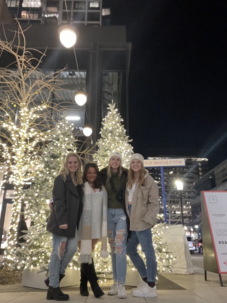 Four friends in front of Christmas trees and outdoor decorations in Boston Massachusetts